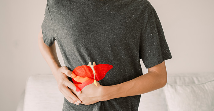 Homem com expressão de dor segurando a lateral do abdômen, com ilustração de um fígado sobreposta à região do corpo.