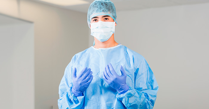 Cirurgião com máscara, touca e roupas esterilizadas em centro cirúrgico, pronto para iniciar um procedimento médico.