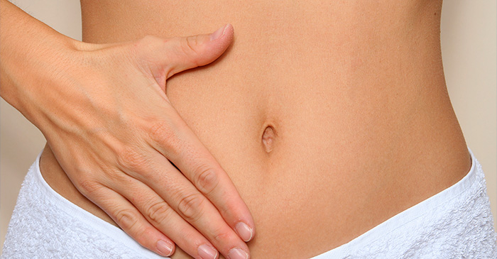 Pessoa com a mão sobre o abdômen inferior, destacando a região umbilical, possivelmente indicando desconforto ou observação de sintomas abdominais.